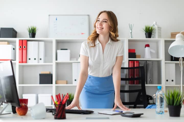 A young woman standing at her desk in an office.