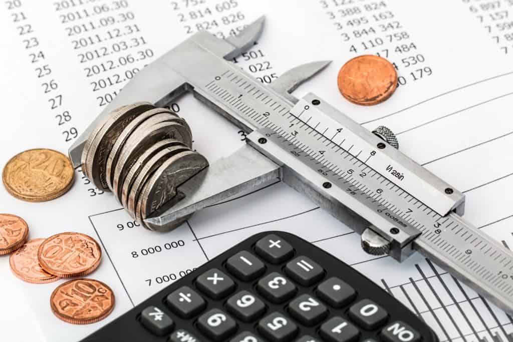 A caliper, calculator and coins on top of a sheet of paper.