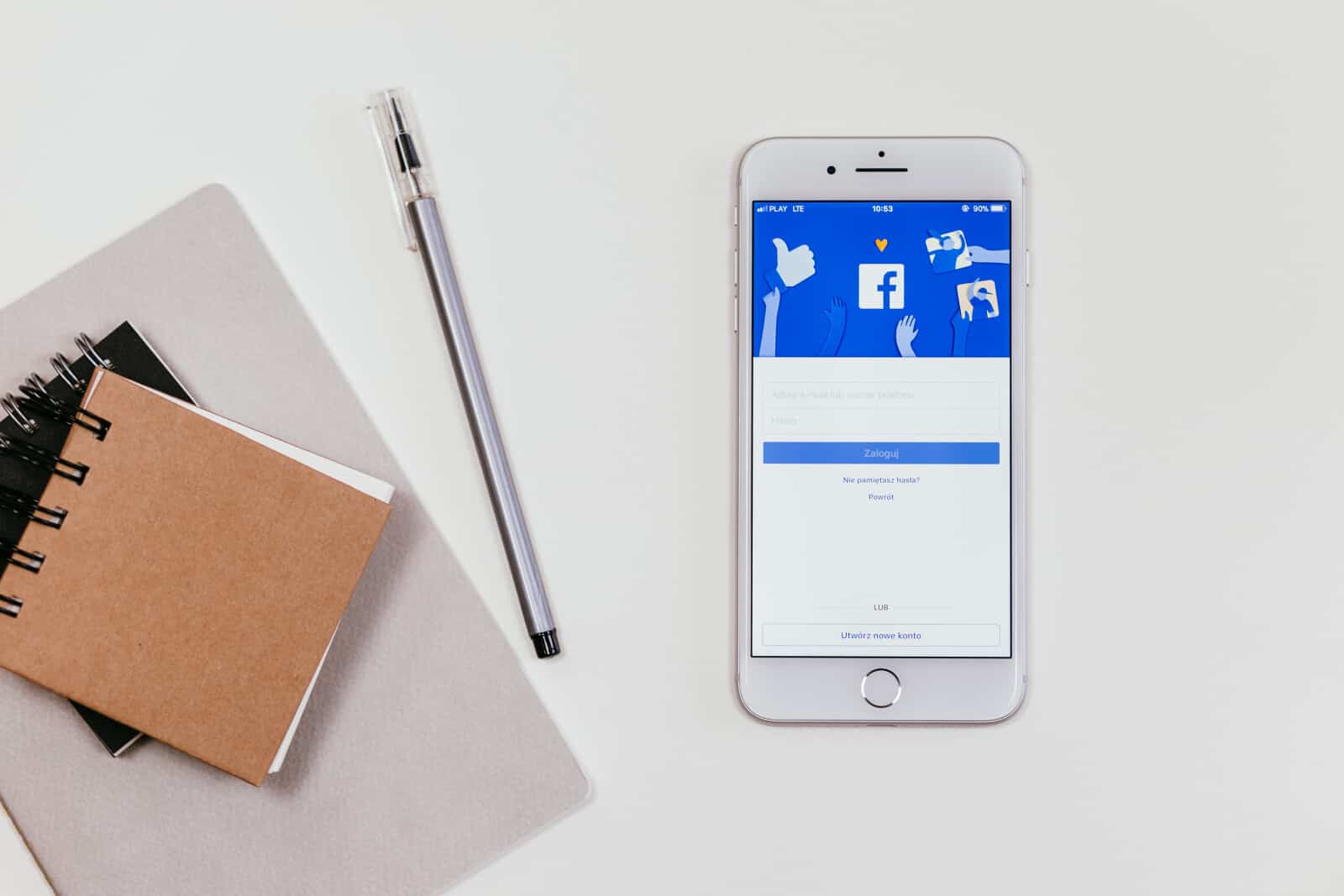 A phone with a facebook app on it next to a notebook.