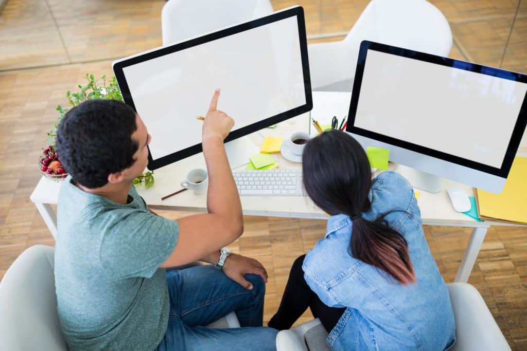 Two people sitting at a desk looking at computer screens.