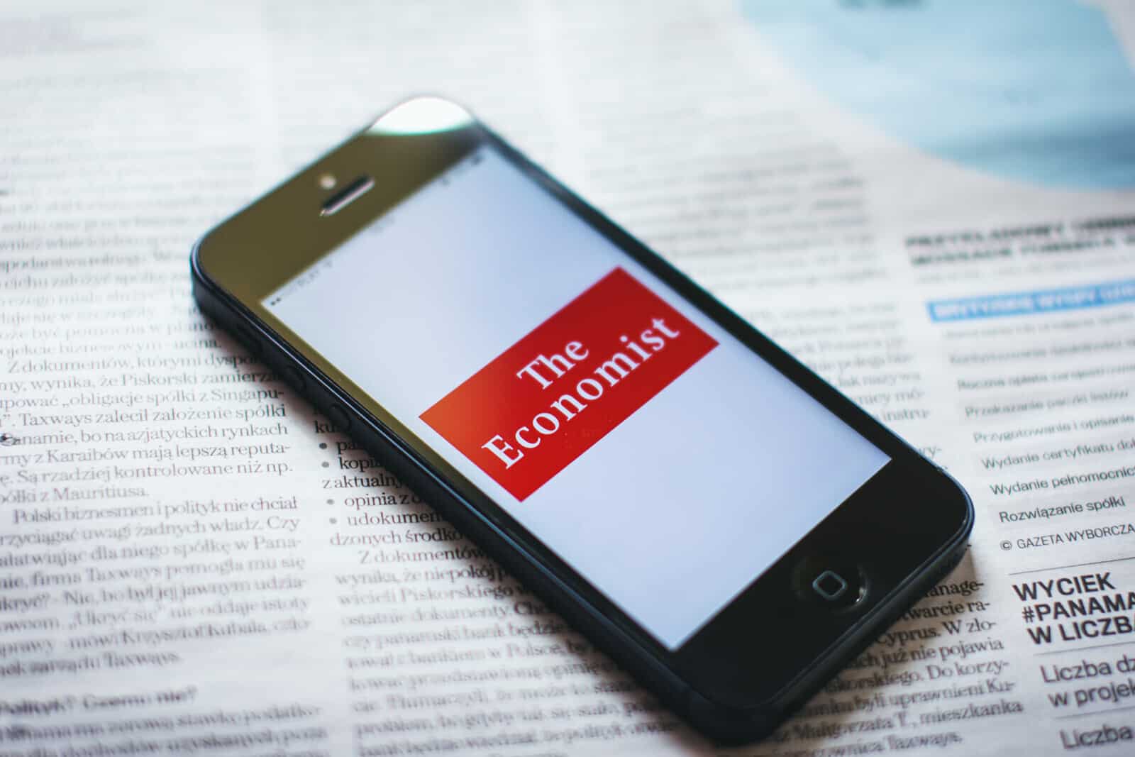 A smartphone with the economist logo on it sitting on top of a newspaper.