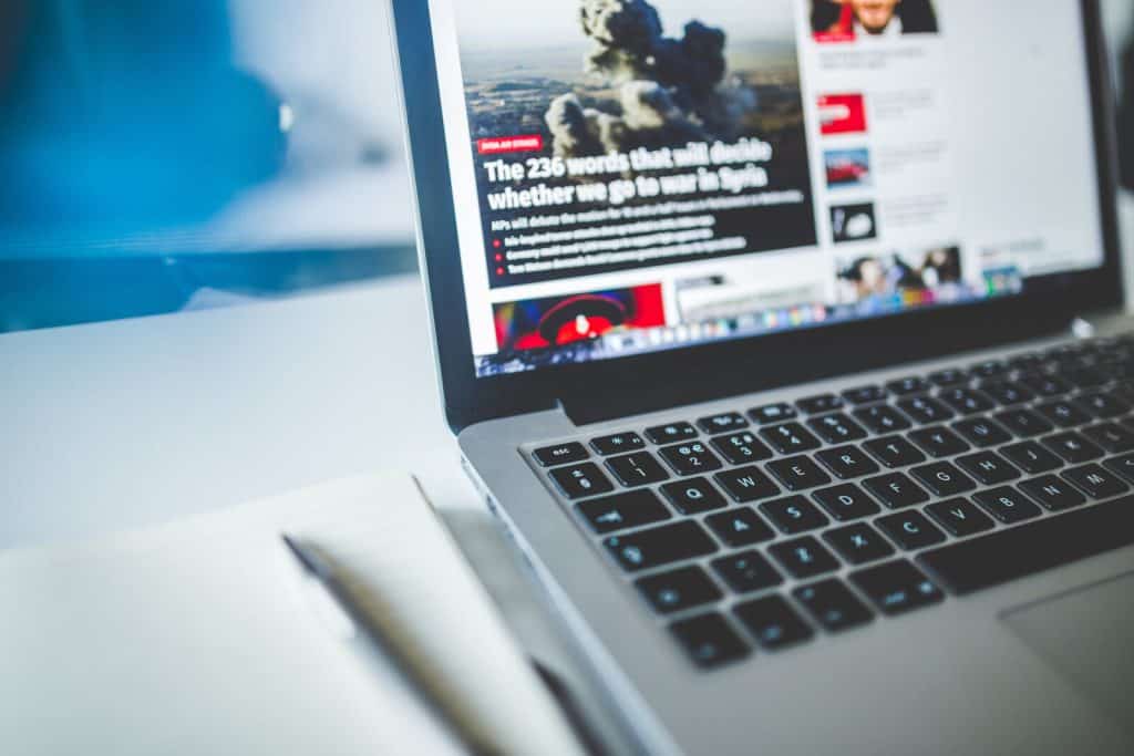 A laptop on a desk with a notepad and pen.